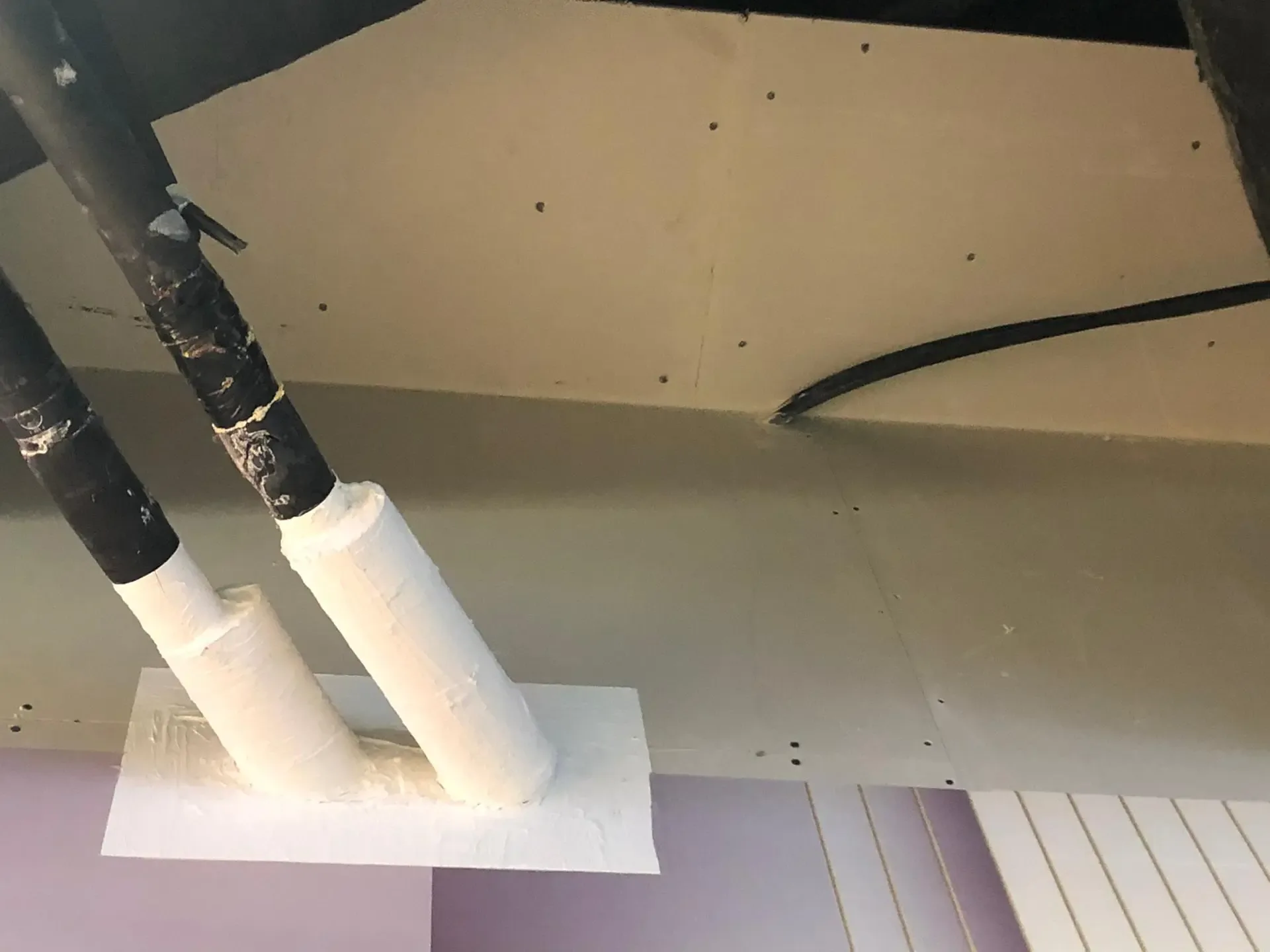 Twee leidingen met witte brandwerende afdichting bij de doorgang door een plafond