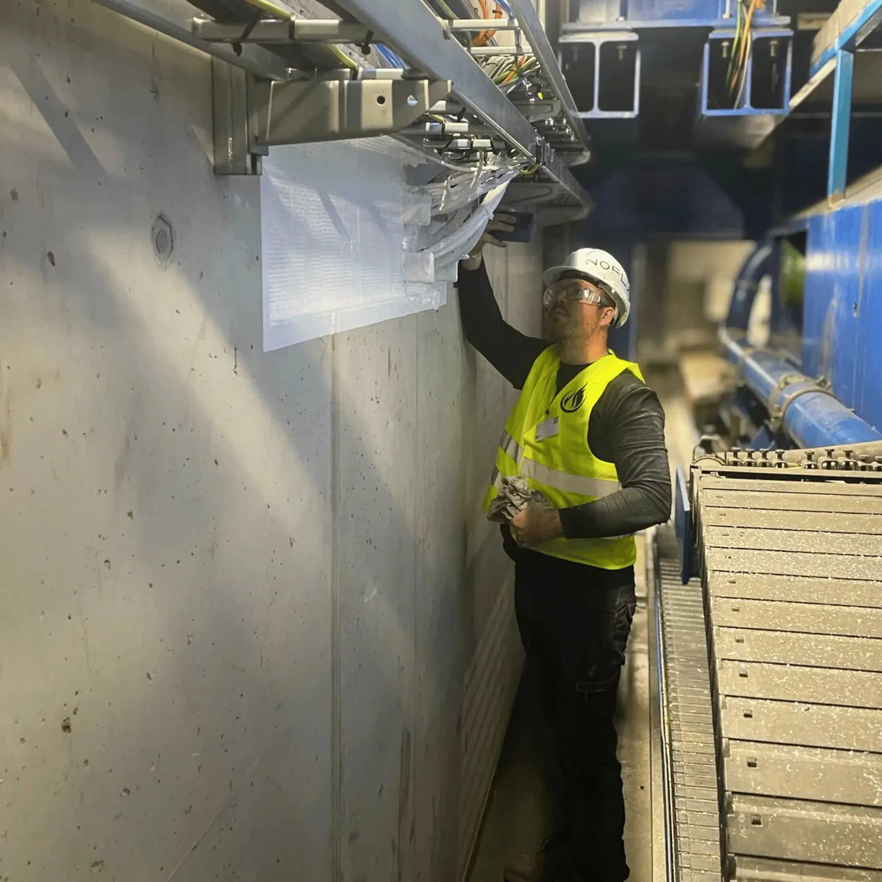 Medewerker in werkkledij bekijkt een kabelgoot die door een wand loopt